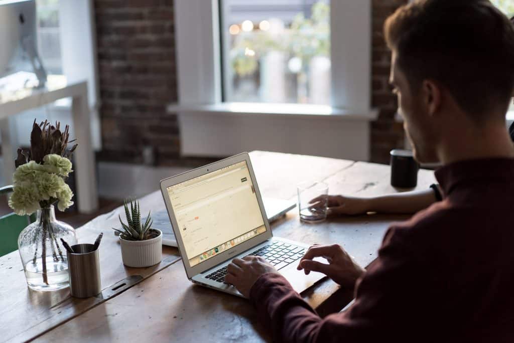 man in brown shirt typing on laptop