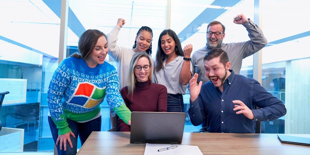 men and women sitting and standing by the table looking happy while staring at laptop happy employees, productive office, success growth