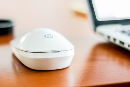 white HP cordless mouse on top of table beside laptop wifi 7, multi link, wireless technology