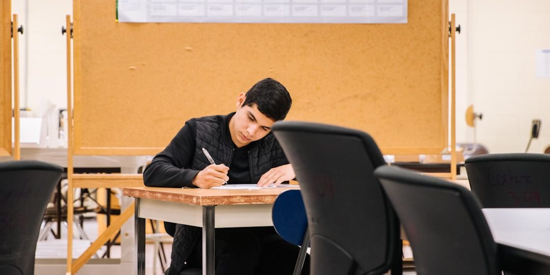 man in black long sleeve shirt sitting on black chair student tutor math books laptop classroom