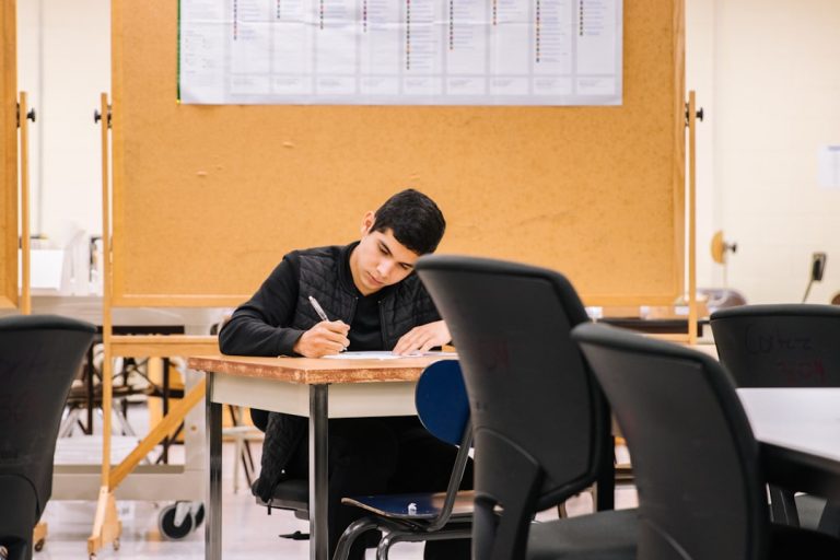 man in black long sleeve shirt sitting on black chair student tutor math books laptop classroom